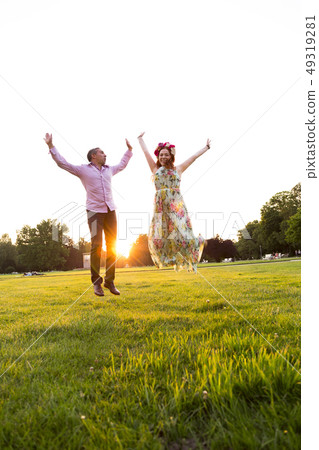 Jumping happy couple on green field in summer park Jumping happy couple on green field in summer park 49319281