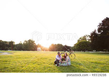 Couple sitting near bicycle at park on summer day Couple sitting near bicycle at park on summer day 49319286