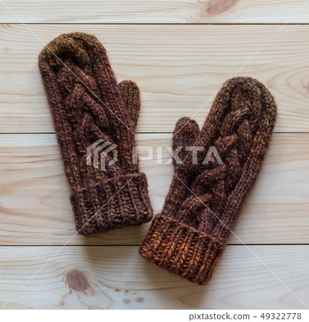 Mittens knitted in dark brown wool on wooden background Mittens knitted in dark brown wool on wooden background 49322778