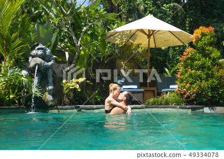 Happy couple kissing while relaxing in outdoor spa infinity swimming pool surrounded with lush 49334078