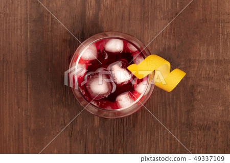 A vibrant red cocktail with campari, an orange curl garnish, and ice cubes, shot from above on a A vibrant red cocktail with campari, an orange curl garnish, and ice cubes, shot from above on a 49337109