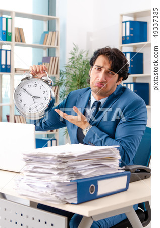 Young handsome male employee with too much work in the office Young handsome male employee with too much work in the office 49337385