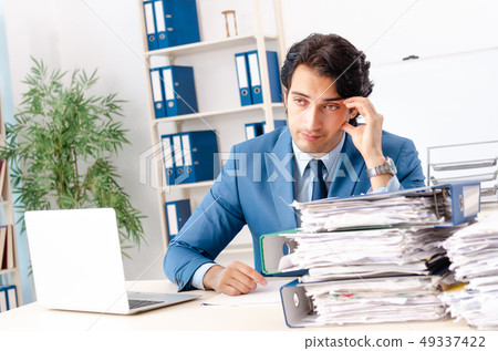 Young handsome male employee with too much work in the office Young handsome male employee with too much work in the office 49337422