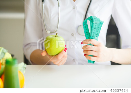 Diet. Female Nutritionist and Holding an Apple and a Measure Tape. New Start For Healthy Nutrition Diet. Female Nutritionist and Holding an Apple and a Measure Tape. New Start For Healthy Nutrition 49337424