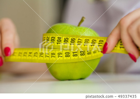 Diet. Woman holding a green apple and measuring Diet. Woman holding a green apple and measuring 49337435