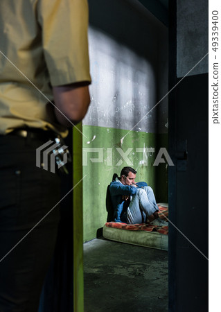 Young male prisoner sitting alone in an obsolete prison cell 49339400