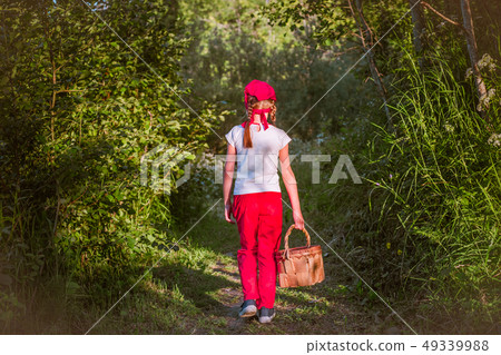 Young girl walking on a path through green woods carrying a basket 49339988