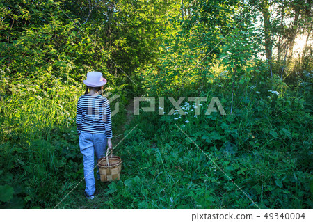 Young girl walking on a path through green woods carrying a basket 49340004