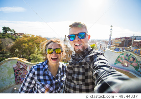 Funny young couple looking at camera taking photo with smart phone smiling in Park Guell, Barcelona Funny young couple looking at camera taking photo with smart phone smiling in Park Guell, Barcelona 49344337