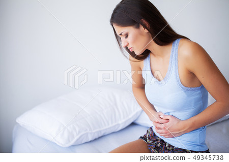 Stomach Pain. Unhealthy young woman with stomachache leaning on the bed at home Stomach Pain. Unhealthy young woman with stomachache leaning on the bed at home 49345738
