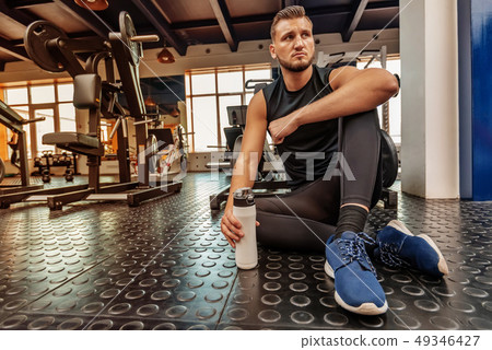 Male athlete sits with fitness drink in modern gym 49346427