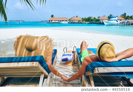 Couple at beach on wooden sun bed loungers 49350519