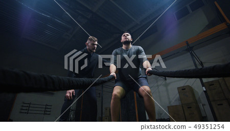 Trainer overseeing young man training with battle rope Trainer overseeing young man training with battle rope 49351254