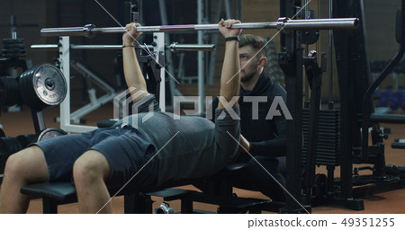 Trainer overseeing young man doing bench press Trainer overseeing young man doing bench press 49351255