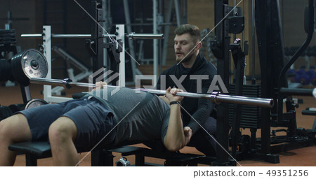 Trainer overseeing young man doing bench press Trainer overseeing young man doing bench press 49351256