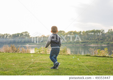 Chilhood, people concept - young boy playing with soap bubbles Chilhood, people concept - young boy playing with soap bubbles 49353447