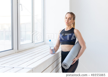 People, sport and fitness concept - young woman with yoga mat and bottle of water standing near 49355865