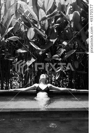 Sensual young woman relaxing in outdoor spa infinity swimming pool surrounded with lush tropical 49370577