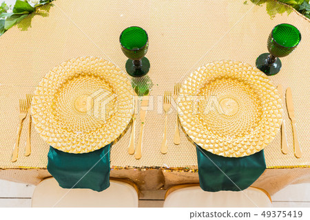 Golden dishes, green wine glasses and napkins. Catering concept. Interior of tent for wedding dinner 49375419