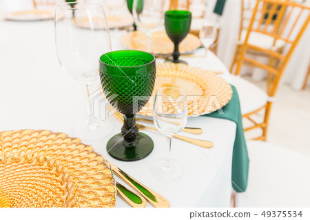 Golden dishes, green wine glasses and napkins. Catering concept. Interior of tent for wedding dinner 49375534