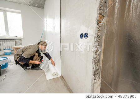 Young man, worker glueing wallpapers on concrete wall. Repair the apartment. Home renovation concept 49375903