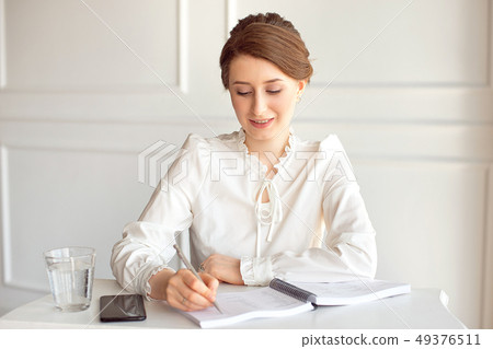 Young woman signs important documents while sitting at her desk in an office. Pretty Caucasian 49376511