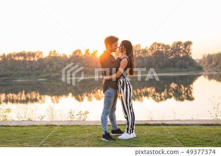 Romantic and people concept - young couple hugging together near the river or lake and enjoying Romantic and people concept - young couple hugging together near the river or lake and enjoying 49377374