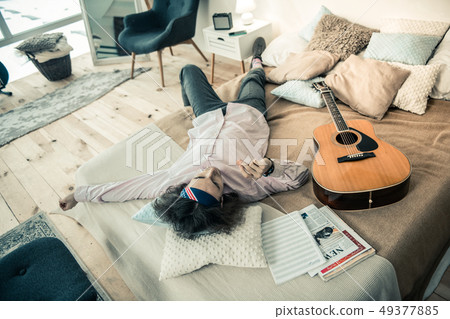 Tired handsome man chilling on covered bed surrounded with pillows 49377885