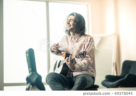 Cheerful handsome young guitarist sitting in bright room 49378045