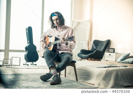 Melancholic handsome musician with wavy hair playing acoustic guitar 49378108