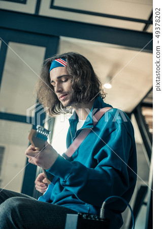 Peaceful handsome young man in bandana focusing on abilities of his instrument Peaceful handsome young man in bandana focusing on abilities of his instrument 49378202