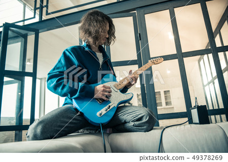 Concentrated young man lying on the back of grey sofa 49378269