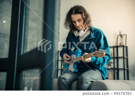 Peaceful good-looking guy with tattoo on the face playing on guitar 49378765