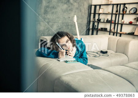 Tired young dark-haired musician leaning on the couch and writing down 49378863