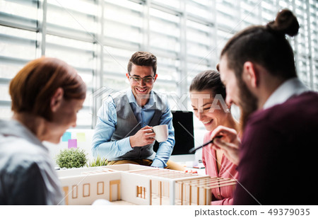 Group of young architects with model of a house working in office, talking. Group of young architects with model of a house working in office, talking. 49379035