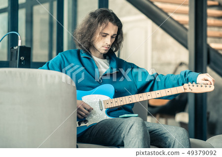 Focused young guitarist with wavy hair setting up musical instrument 49379092