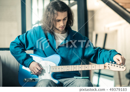 Concentrated good-looking unusual guy setting up strings on his electronic guitar 49379183