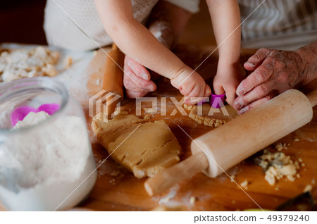 Midsection of grandmother with small toddler boy making cakes at home. 49379240