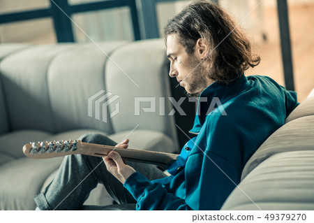 Focused dark-haired man with stubble peacefully playing on guitar 49379270