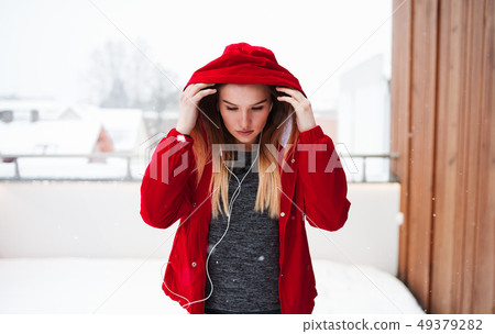 A portrait of young girl or woman with earphones outdoors, listening to music. 49379282