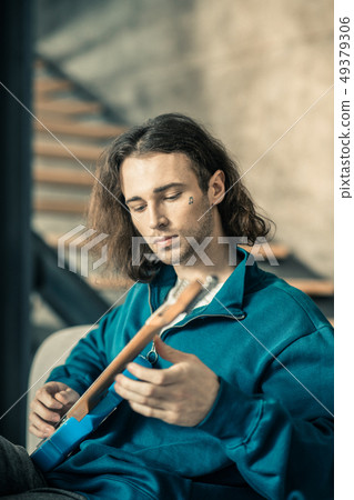 Careless good-looking young man toning strings on his guitar 49379306