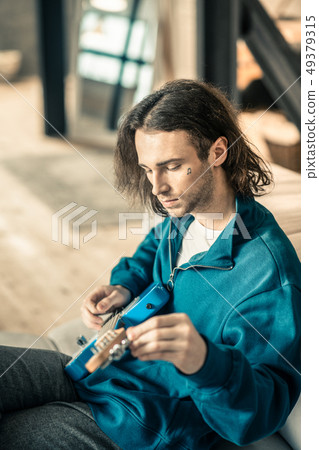 Melancholic young man in blue sweatshirt setting up his musical instrument 49379315