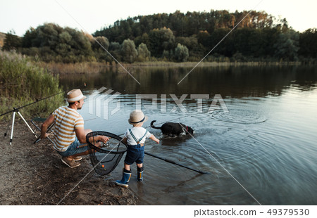 A mature father with a small toddler son and dog outdoors fishing by a lake. 49379530
