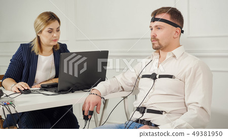 polygraph technician reads questions from a laptop. man connected to the lie detector circuit 49381950