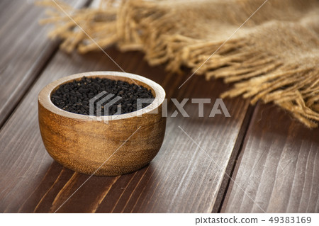 Black cumin seeds on brown wood Black cumin seeds on brown wood 49383169
