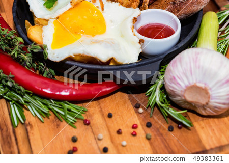 Nutricious meal with fried egg, onion rings, chili pepper and sauce in frying pan Nutricious meal with fried egg, onion rings, chili pepper and sauce in frying pan 49383361