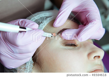 Permanent Makeup For Eyebrows. Microblading brow. Beautician Doing Eyebrow Tattooing For Female Face Permanent Makeup For Eyebrows. Microblading brow. Beautician Doing Eyebrow Tattooing For Female Face 49384618