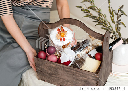 Wooden gift box in female hands with spring flowers on light natural fabric background. Easter 49385244