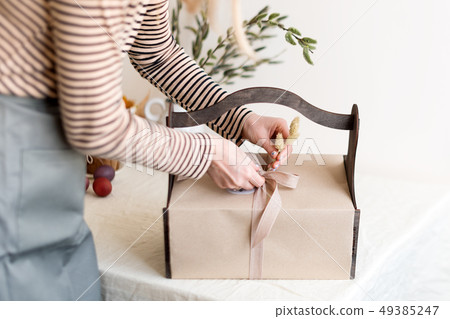 Wooden gift box in female hands with spring flowers on light natural fabric background. Easter 49385247