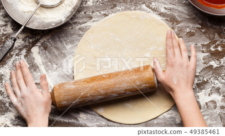 Woman preparing dough for pizza on table, top view 49385461